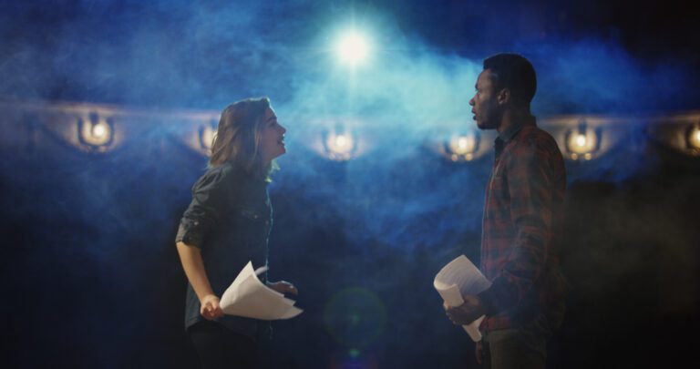 Two actors, dressed in flannel shirts, rehearsing a n intense scene on stage, scripts in-hand.